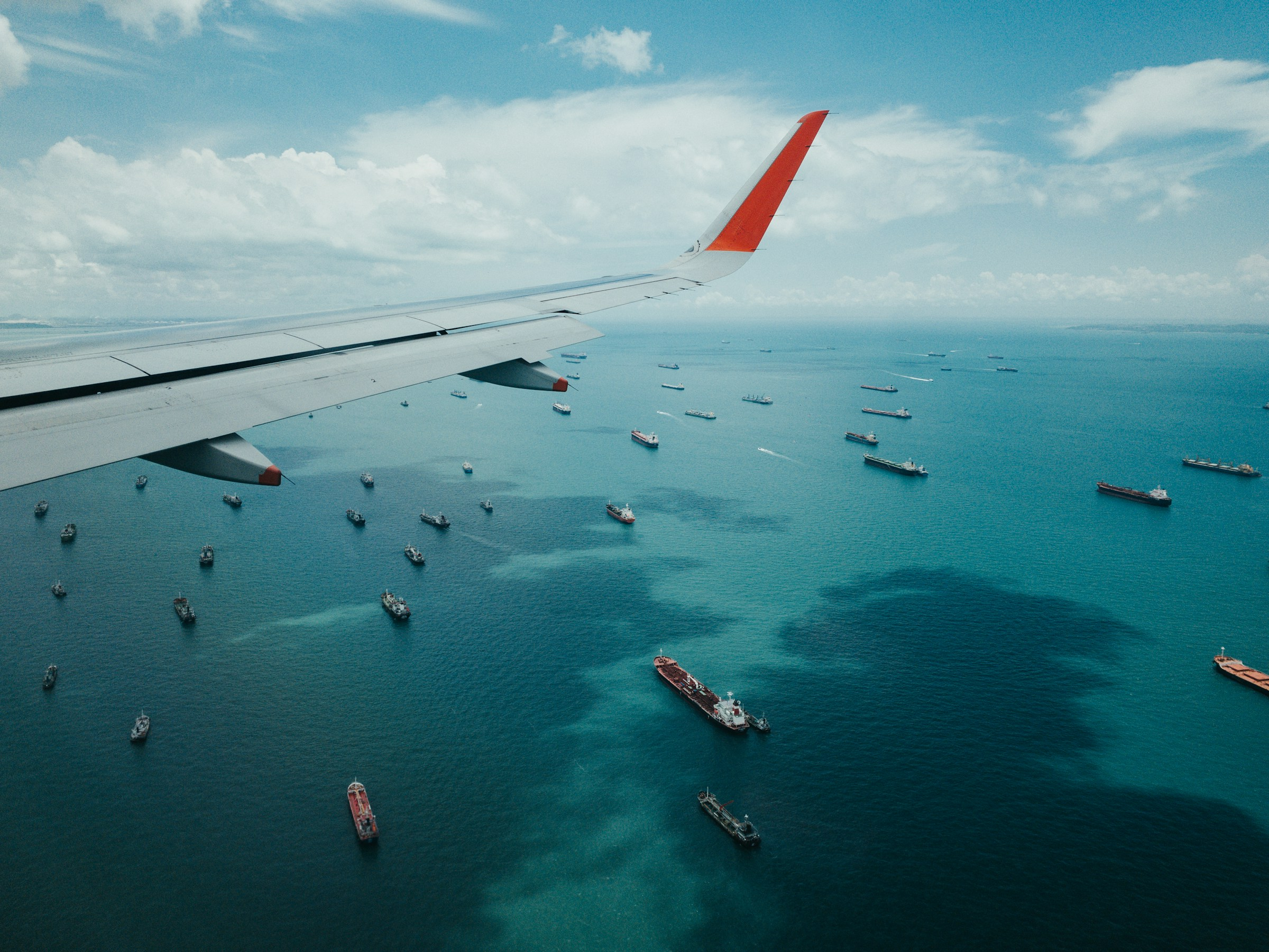 Airplane wing over the sea near the Port of Singapore, representing PayQuid global trade reach